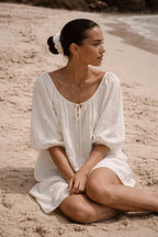 Woman in a white Atoll sundress sitting on a sandy beach