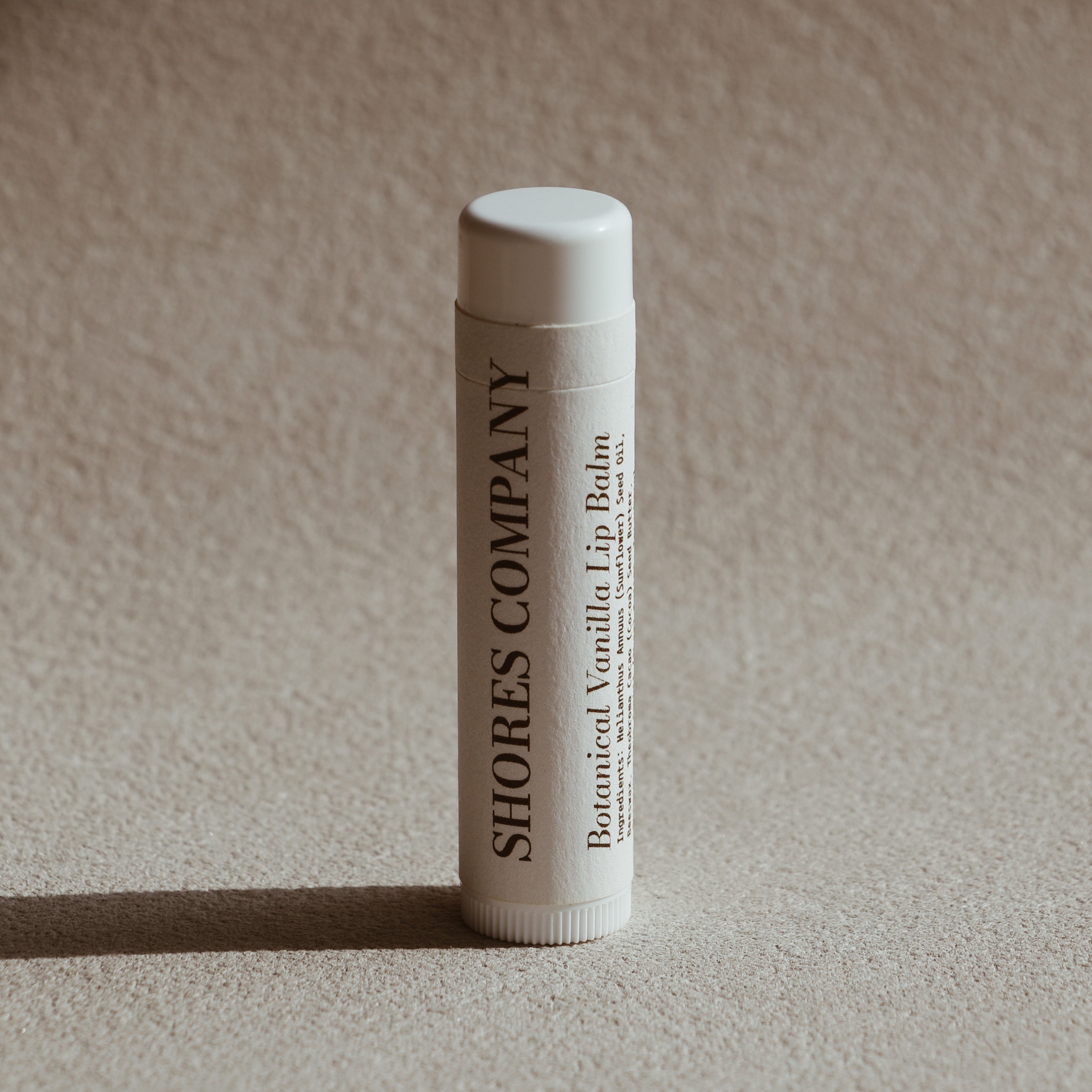 Lip balm tube with 'Shores Company' branding on a beige background