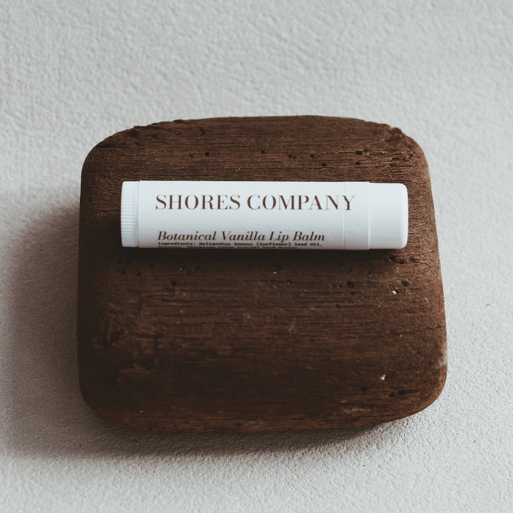 Lip balm on a wooden block with 'Shores Company' label on a light gray background