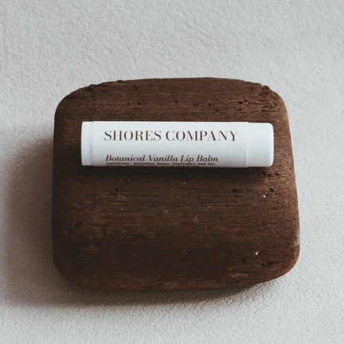 Lip balm on a wooden block with 'Shores Company' label on a light gray background
