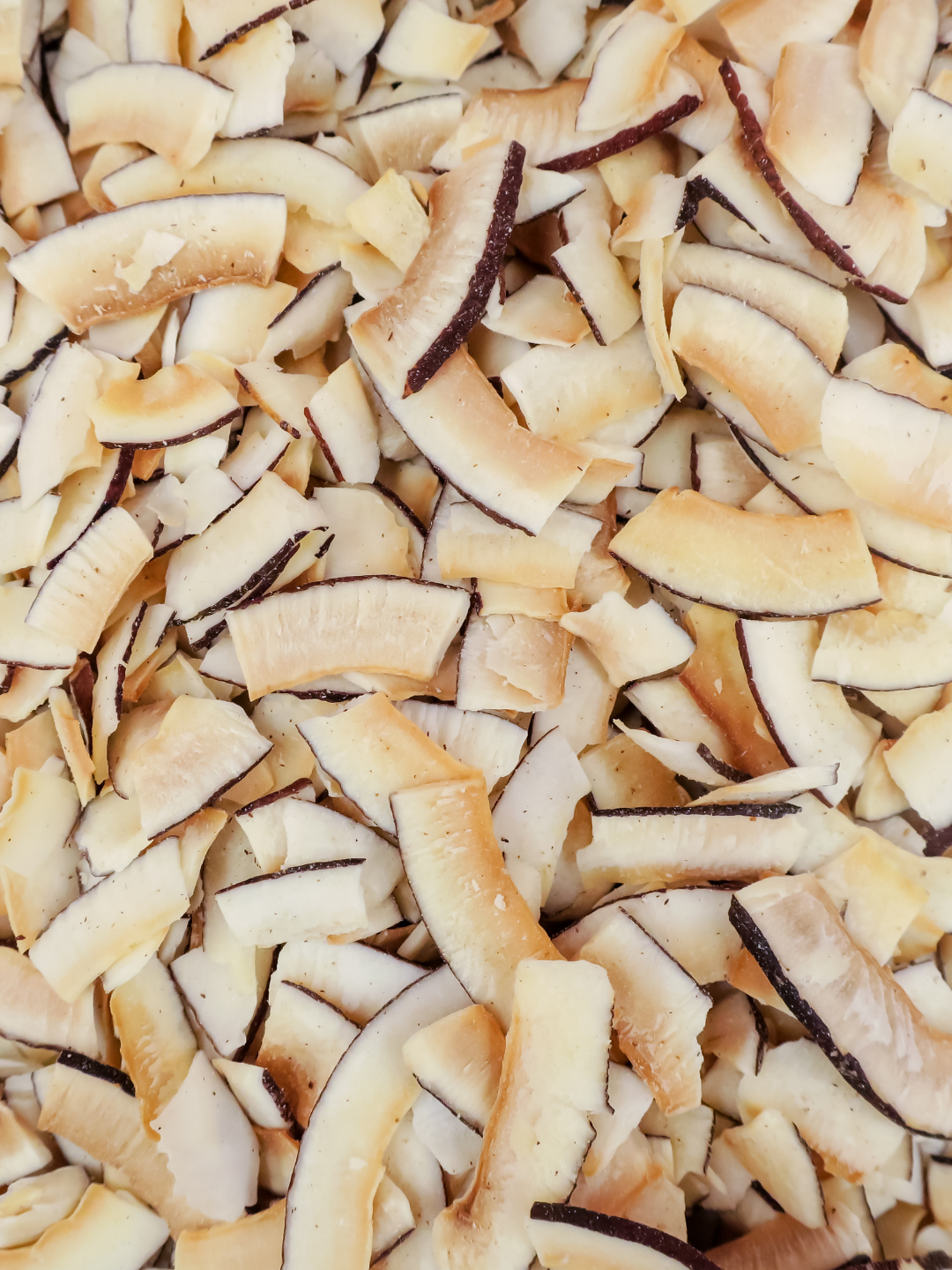 A close-up view of shredded dried coconut flakes filling the frame, showing pale beige and cream layers with darker brown edges.