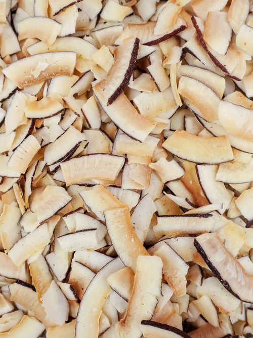 A close-up view of shredded dried coconut flakes filling the frame, showing pale beige and cream layers with darker brown edges.
