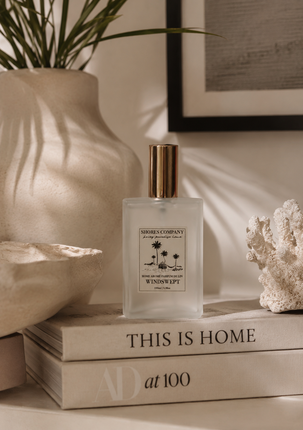 A frosted glass perfume bottle with a gold cap and a vintage-style label reading 'SIRI'S COMPANY' and 'WINDSWEEP', styled on stacked books in a warm, sunlit interior setting.