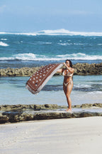 Woman  on a rocky beach with ocean waves in the background holding Isle pareo