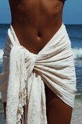 Person wearing a white sarong on a beach with ocean in the background