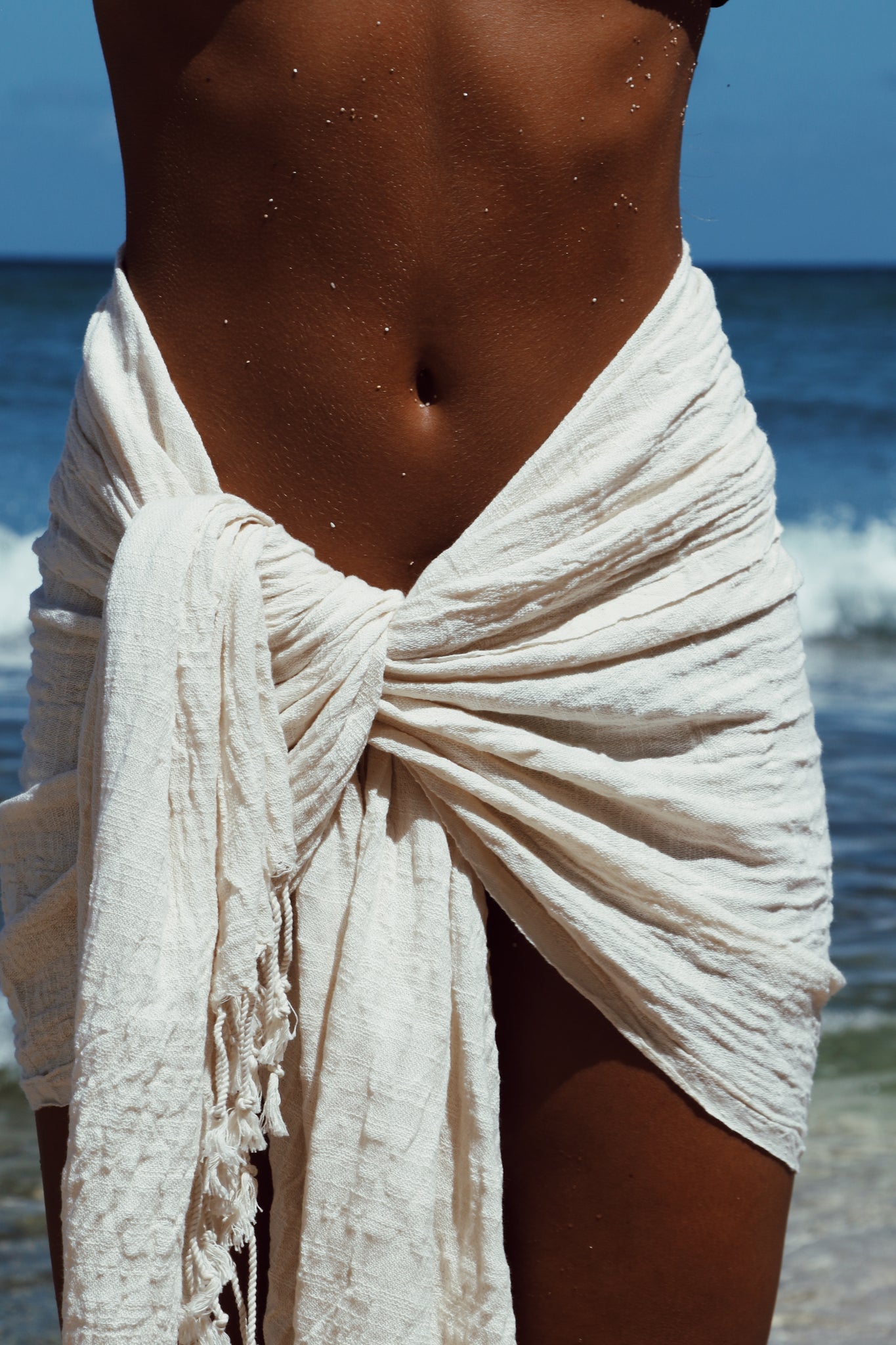Person wearing a white sarong on a beach with ocean in the background