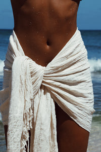 Person wearing a white sarong on a beach with ocean in the background