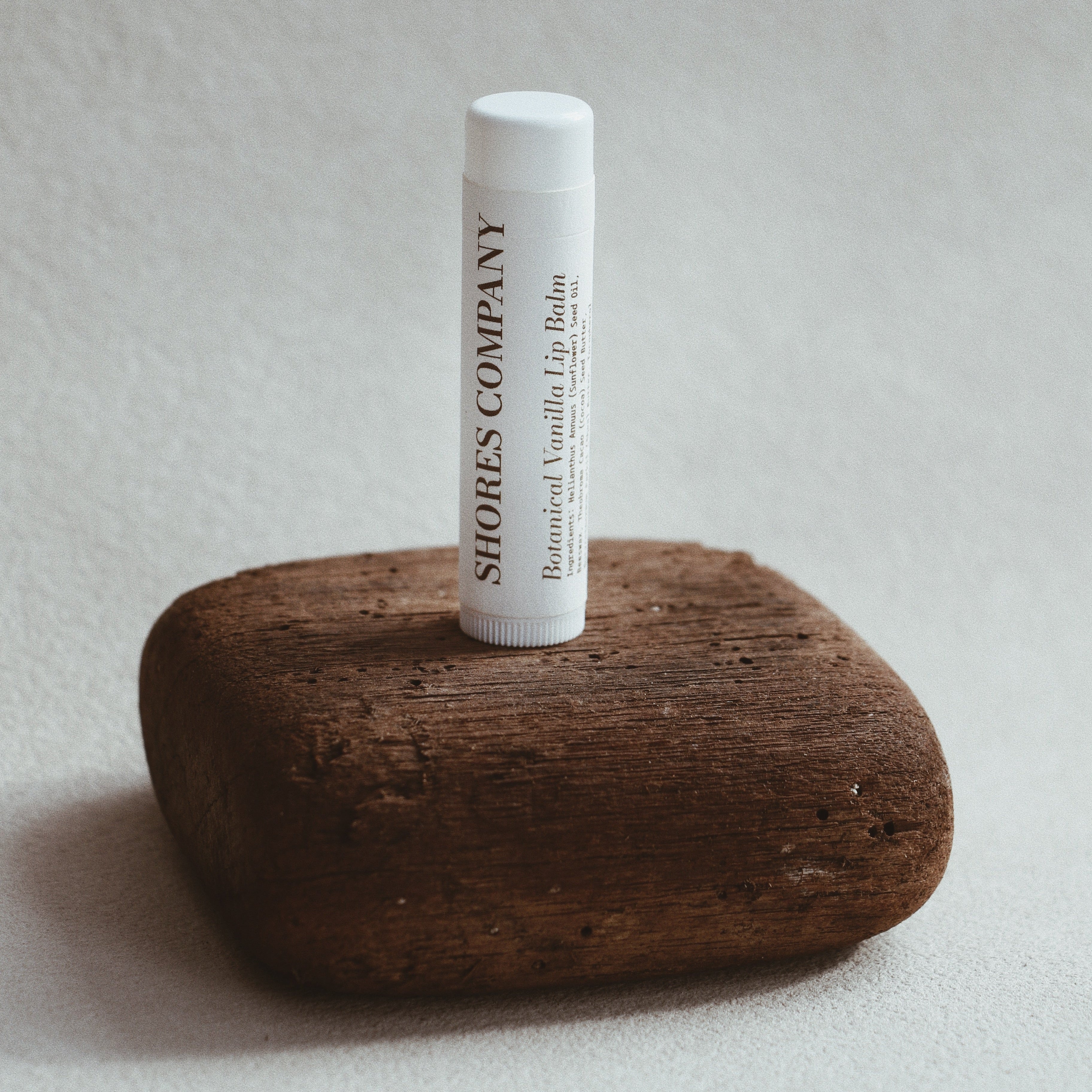 Shores Co lip balm tube on a wooden block with a neutral background