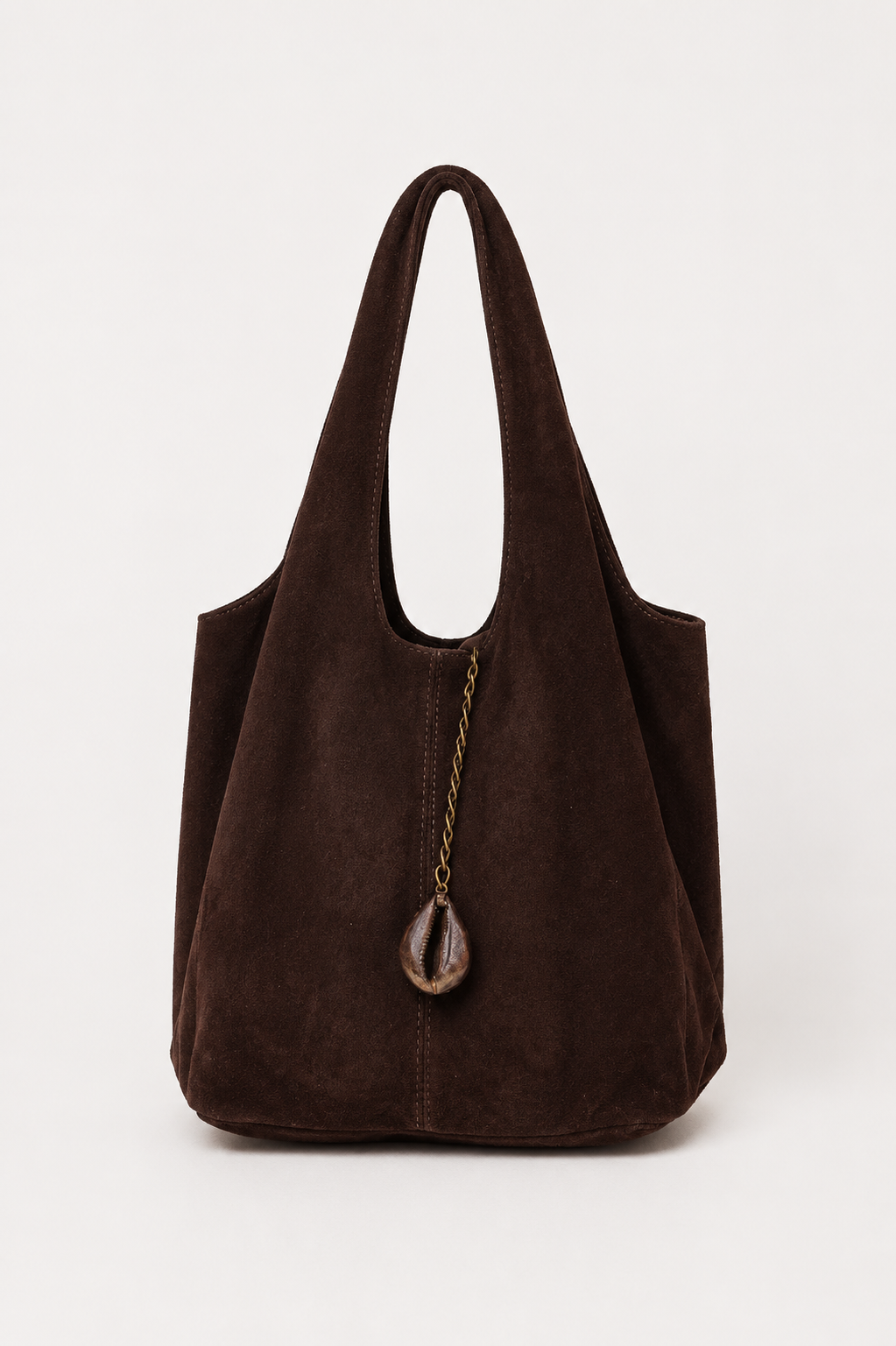 A dark brown suede hobo-style tote bag with a single shoulder strap and a decorative cowrie charm hanging from a gold-tone chain, shown against a plain light background.