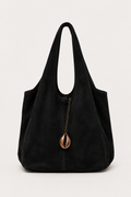 A black suede hobo shoulder bag with a decorative bronze cowrie shell charm hanging from a chain zipper, set against a plain light gray background.