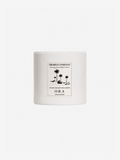 A white ceramic candle jar with a minimalist black graphic label reading 'Shores Company' and 'ORA', set against a solid white background.