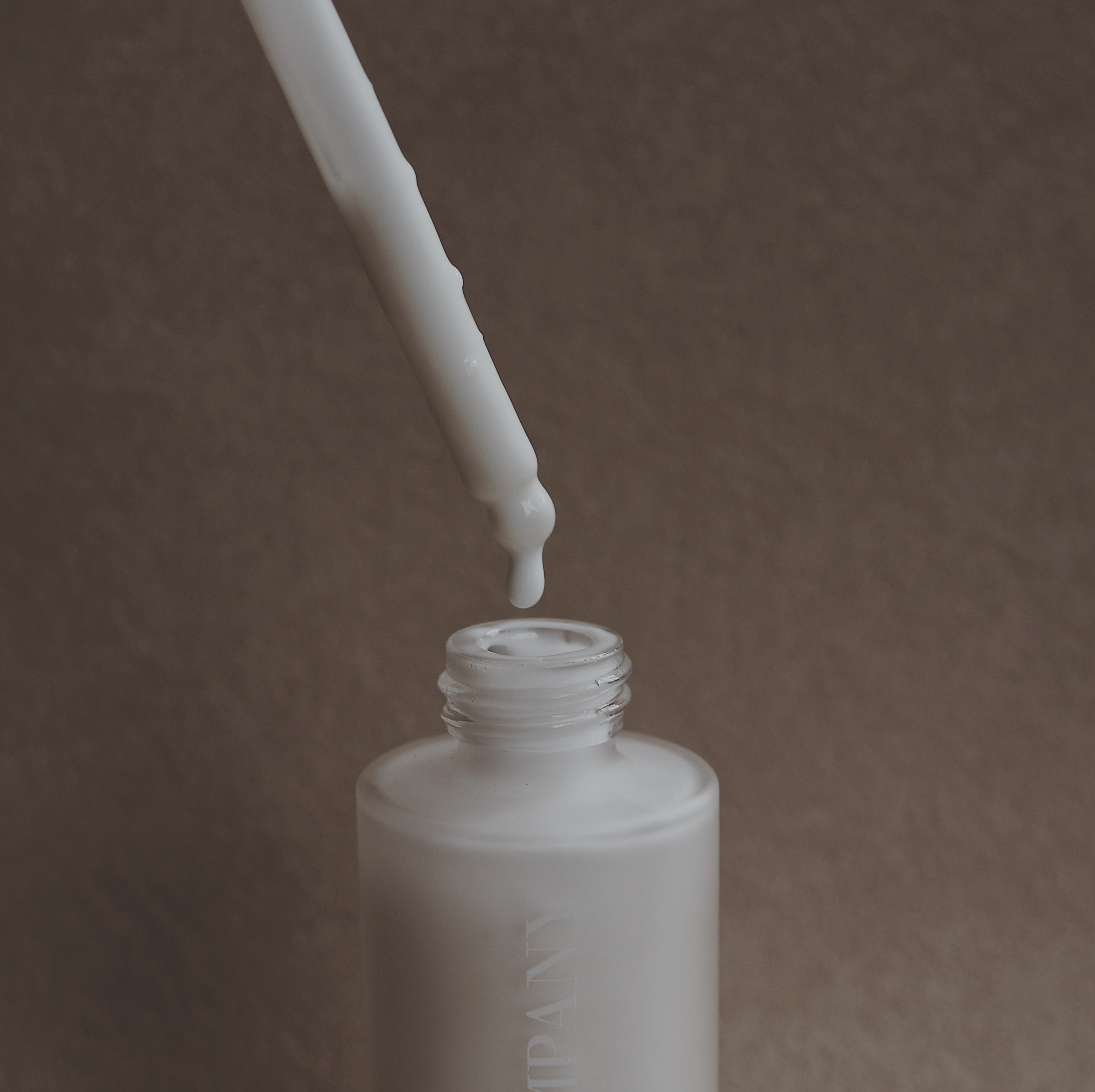 Goat Milk Cleanser White dropper bottle with a dropper on a brown background