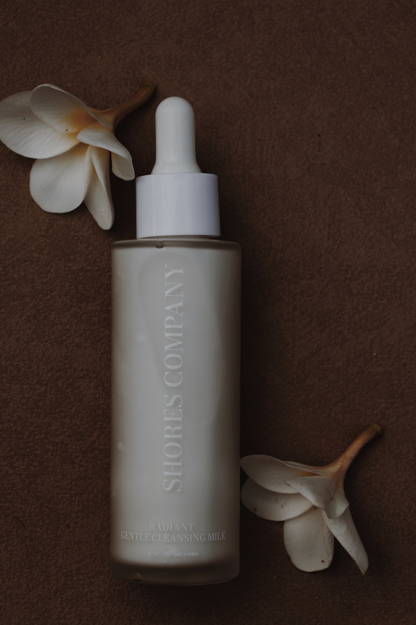 Shores Company Skincare bottle with dropper on a brown background with flowers