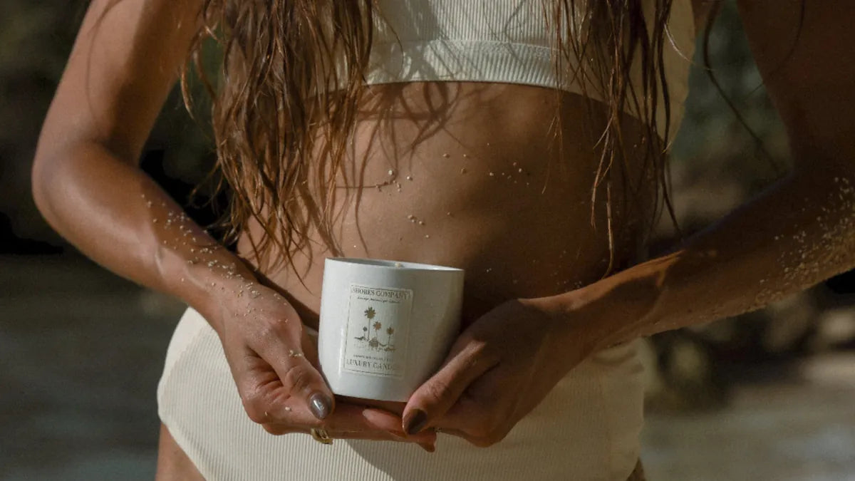 Person holding a Shores candle on the beach