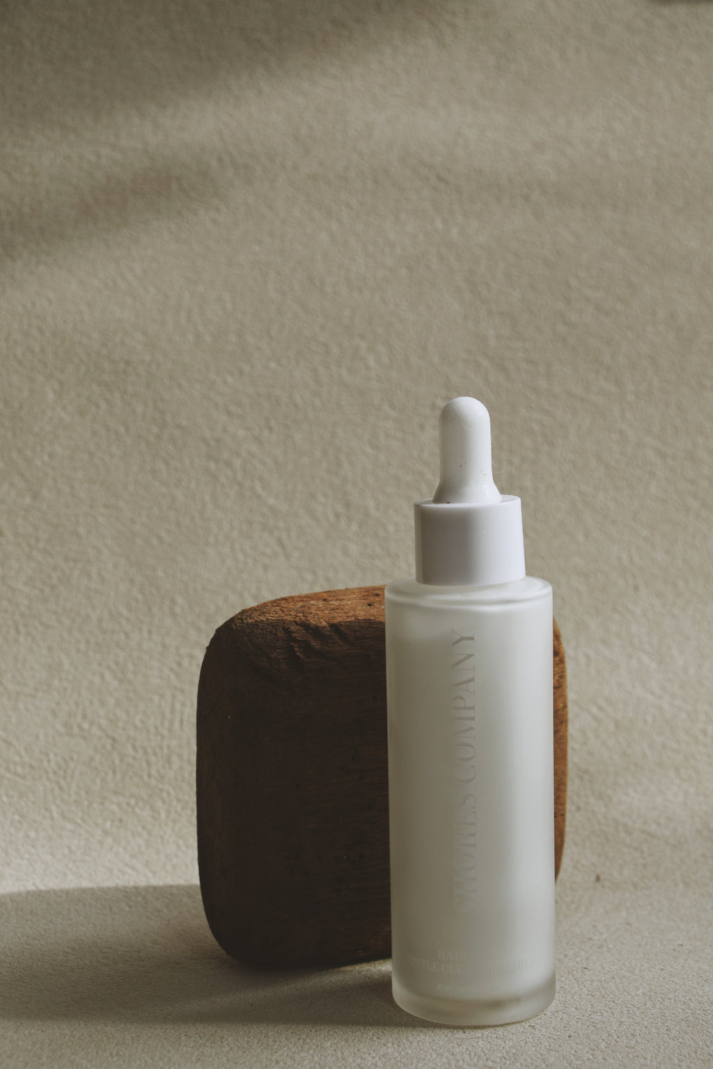 White dropper bottle with wooden base on a beige background