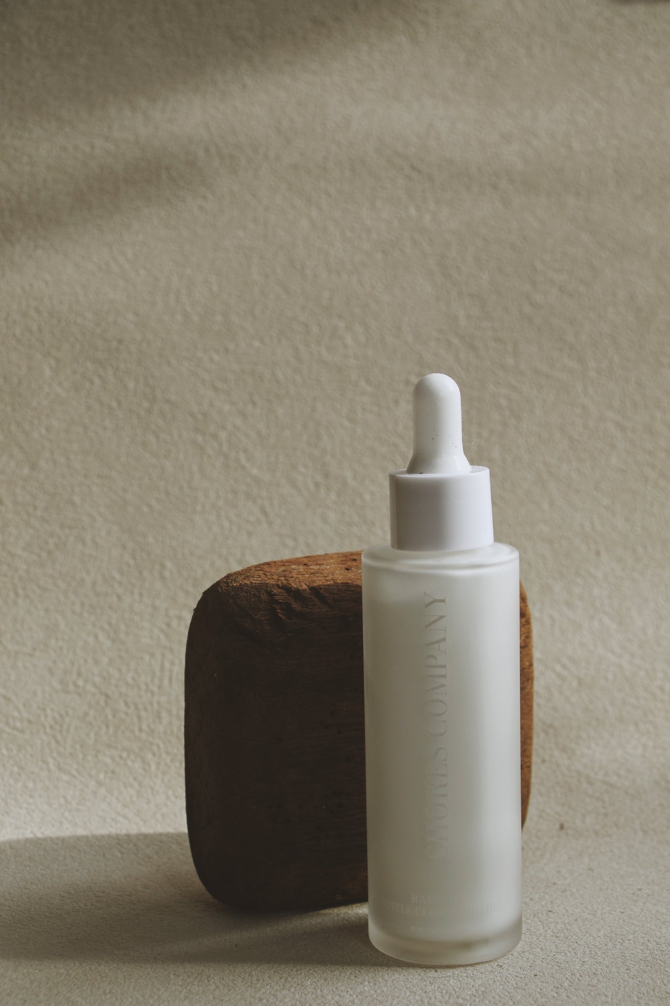 White dropper bottle with wooden base on a beige background