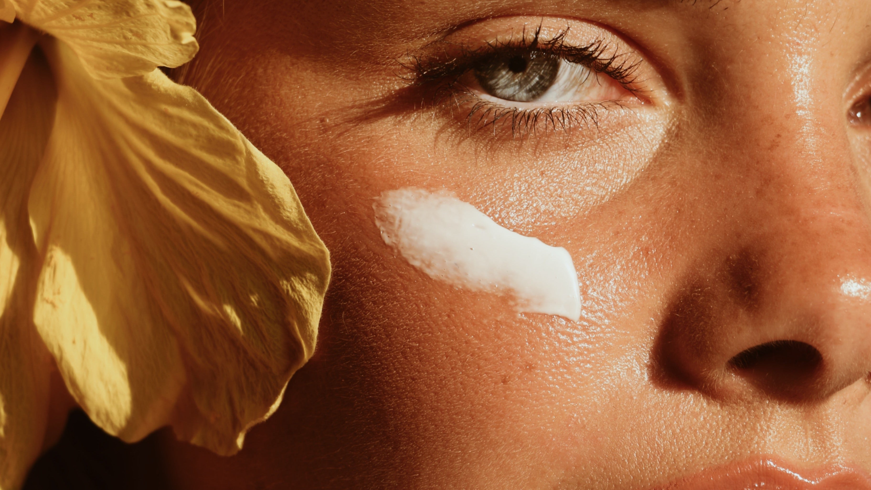 Close-up of a woman's face with a yellow flower in her hair, sun-kissed skin.