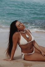 Woman in a Vai white bikini sitting on the beach with ocean waves in the background