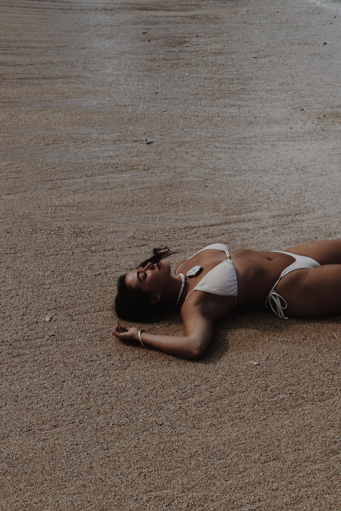 Woman lying on sand wearing Vai white bikini