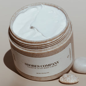 Open jar of Shores Company Coastal Luxe Body Crème, showcasing its rich, whipped texture. A deeply hydrating body moisturizer infused with coconut oil and shea butter.