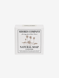 A white rectangular box of Shores Company Natural Soap, featuring a minimalist black and brown tropical illustration of palm trees and a hut on the front label.
