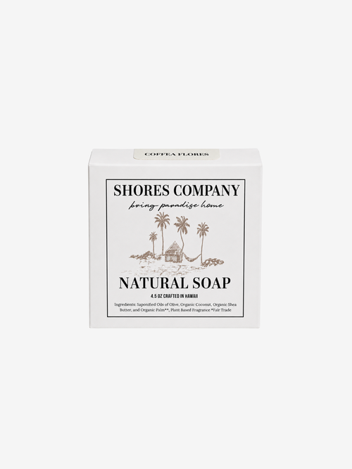 A white rectangular box of Shores Company Natural Soap, featuring a minimalist black and brown tropical illustration of palm trees and a hut on the front label.