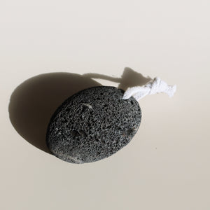 A natural black lava pumice stone with a cotton rope loop, sourced sustainably in Haleiwa, ideal for eco-conscious exfoliation.