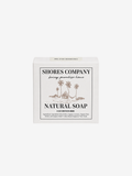 A white rectangular box of Shores Company Natural Soap, featuring a black and brown tropical beach illustration on the front label, set against a plain light gray background.