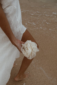 A pair of hands gently holding a handcrafted bath sponge, with water droplets falling into the ocean.