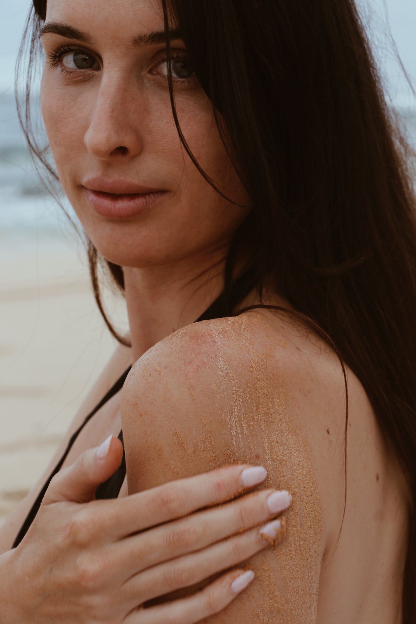 Woman applying Shores Company Driftwood Body Polish to her shoulder for deep exfoliation and skin renewal, made with natural, eco-friendly ingredients.