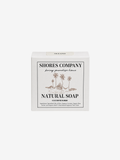 A white rectangular box of Shores Company Natural Soap, featuring a minimalist black and beige illustration of palm trees on the front label, set against a solid light gray background.