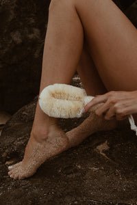 A woman exfoliating her legs with a natural dry brush, a self-care essential for smooth skin.