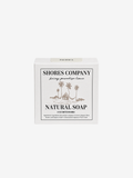 A white rectangular box of Shores Company Natural Soap, featuring a minimalist black and brown tropical illustration of palm trees and a hut on the front label, set against a solid light gray background.