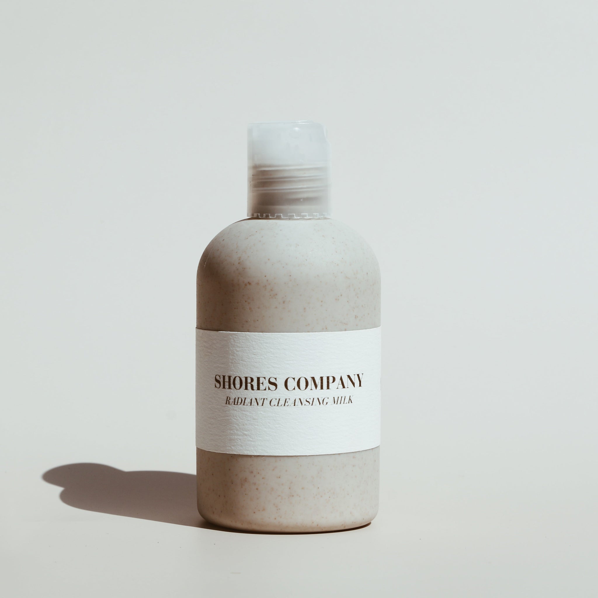 Shores Company Radiant Cleansing Milk bottle placed on a neutral background with soft shadows and natural elements.