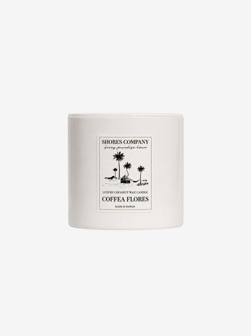 A white ceramic jar candle with a black printed label reading 'Shores Company' and 'Coffea Flores' with a palm tree illustration, centered on a light gray background.