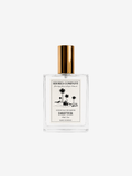 A clear glass perfume bottle with a metallic gold cap and a cream-colored label featuring black palm tree illustrations. The label reads 'SHORES COMPANY' and 'DRIFTER'.