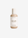 A bottle of Shore's Company Escape Hand & Body Wash, featuring a beige body and a white cap, centered on a light gray background.