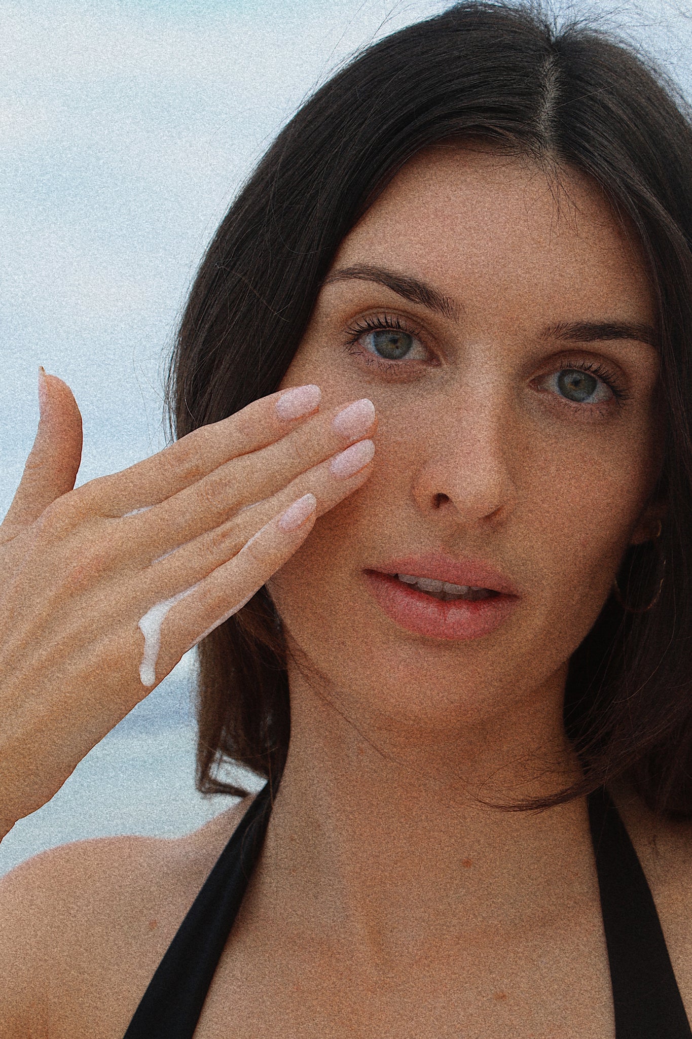 A woman holding Shores Company Radiant Cleansing Milk on a Haleiwa beach, highlighting this natural, Hawaii-inspired skincare essential.